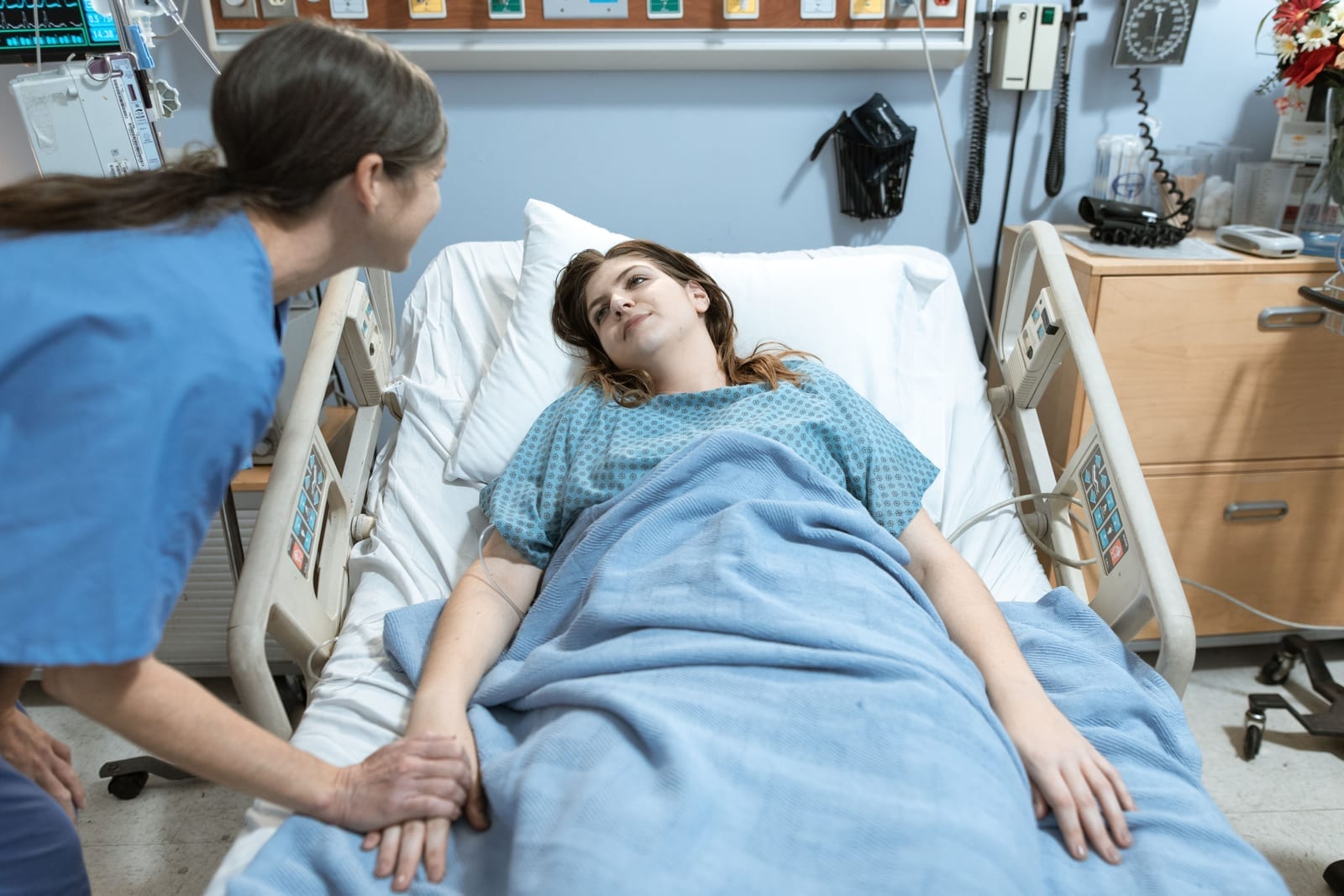 A nurse holding a patient's hand in a hospital room