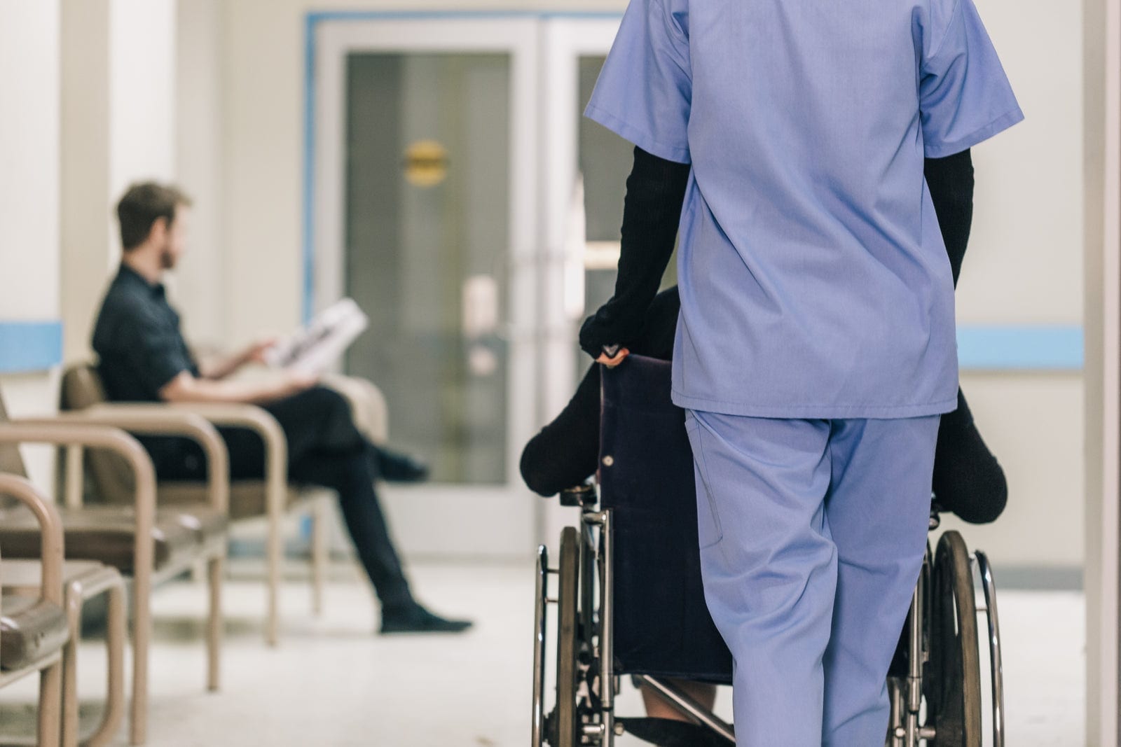 A healthcare worker pushing a patient in a wheelchair through a hospital corridor