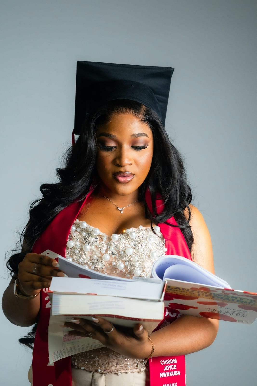 A new nursing graduate in cap and gown holding a stack of books