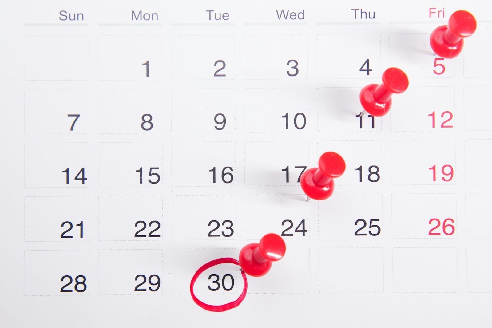 A paper calendar marked with red push pins on several dates