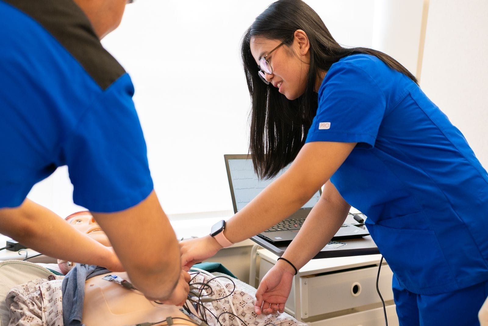 Nursing students in a simulation lab practicing hands-on skills with a training mannequin