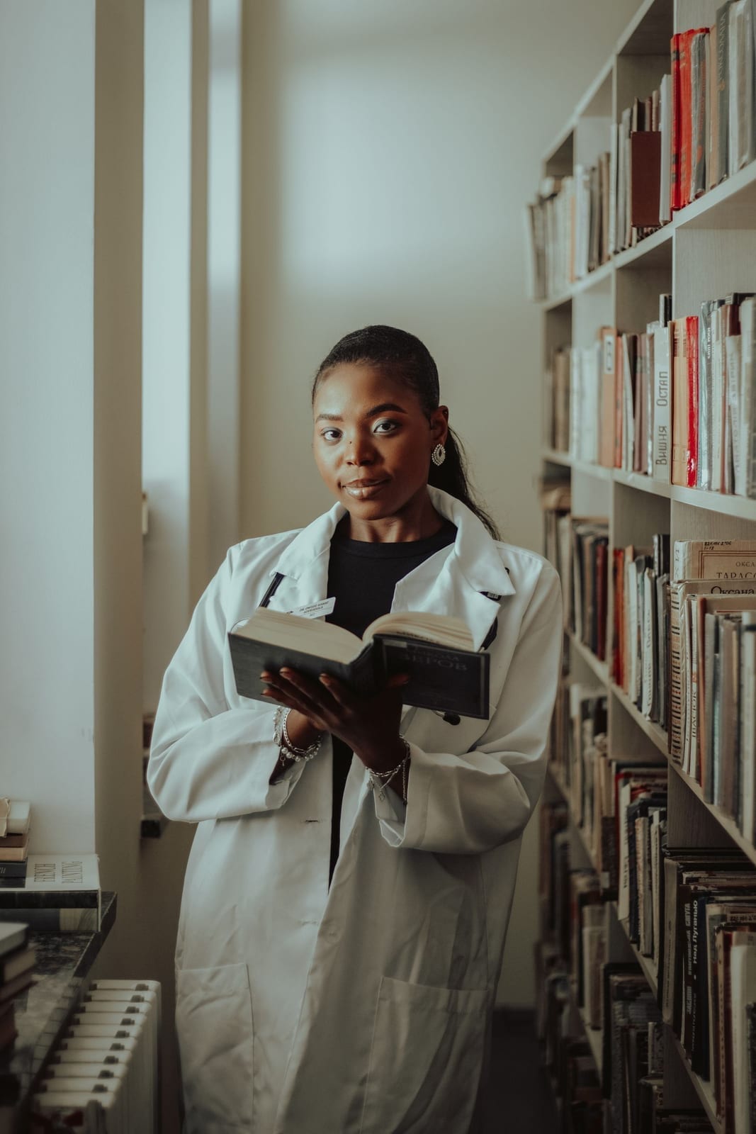 A person in a lab coat reading a book in a library setting