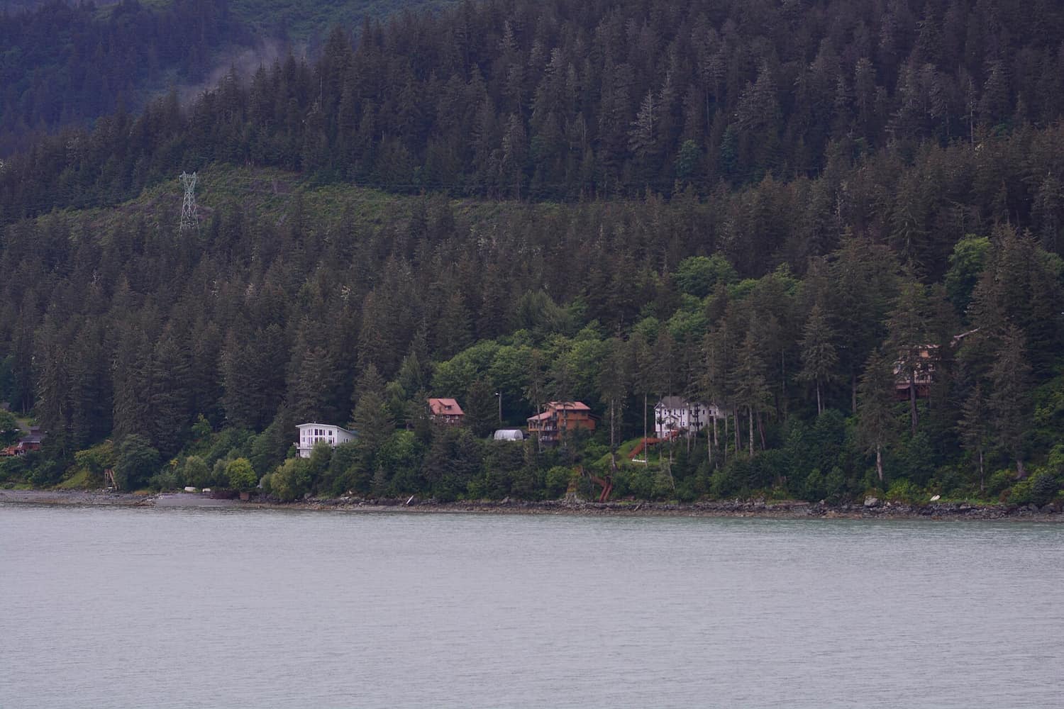 Wooden houses stacked along the steep shoreline of southeast Juneau, Alaska, with forest rising behind them