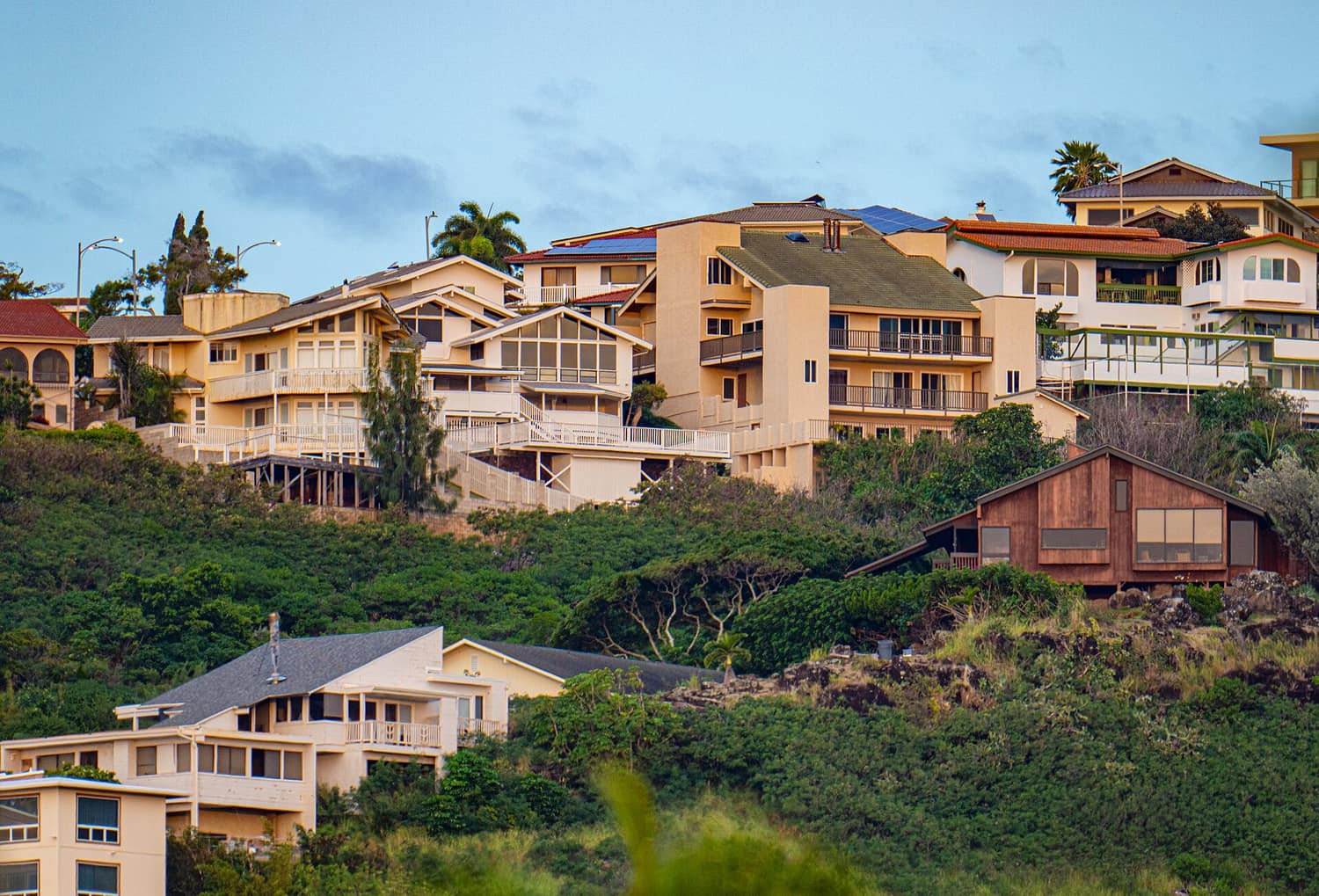 Single-family houses stepping up a green hillside above Oahu, Hawaii, with the ocean in the distance