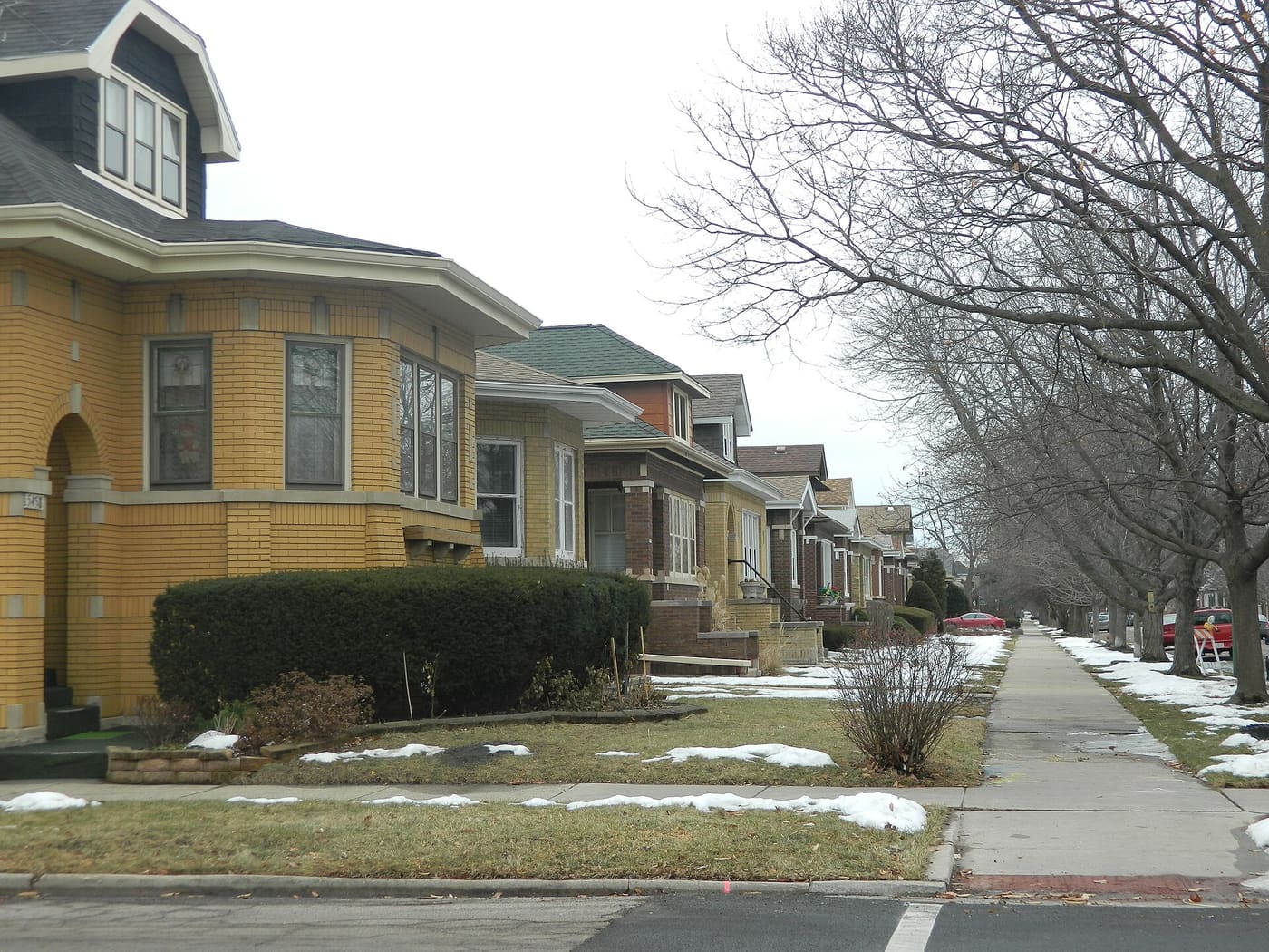 A row of brick Chicago bungalows with front porches along a residential street